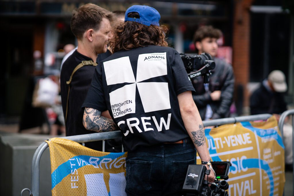 Man holding a camera whilst looking at another man's camera, by a multi coloured barrier in Ipswich. Both are working for Greyhound Creative, Suffolk's Creative Agency, Suffolk videography